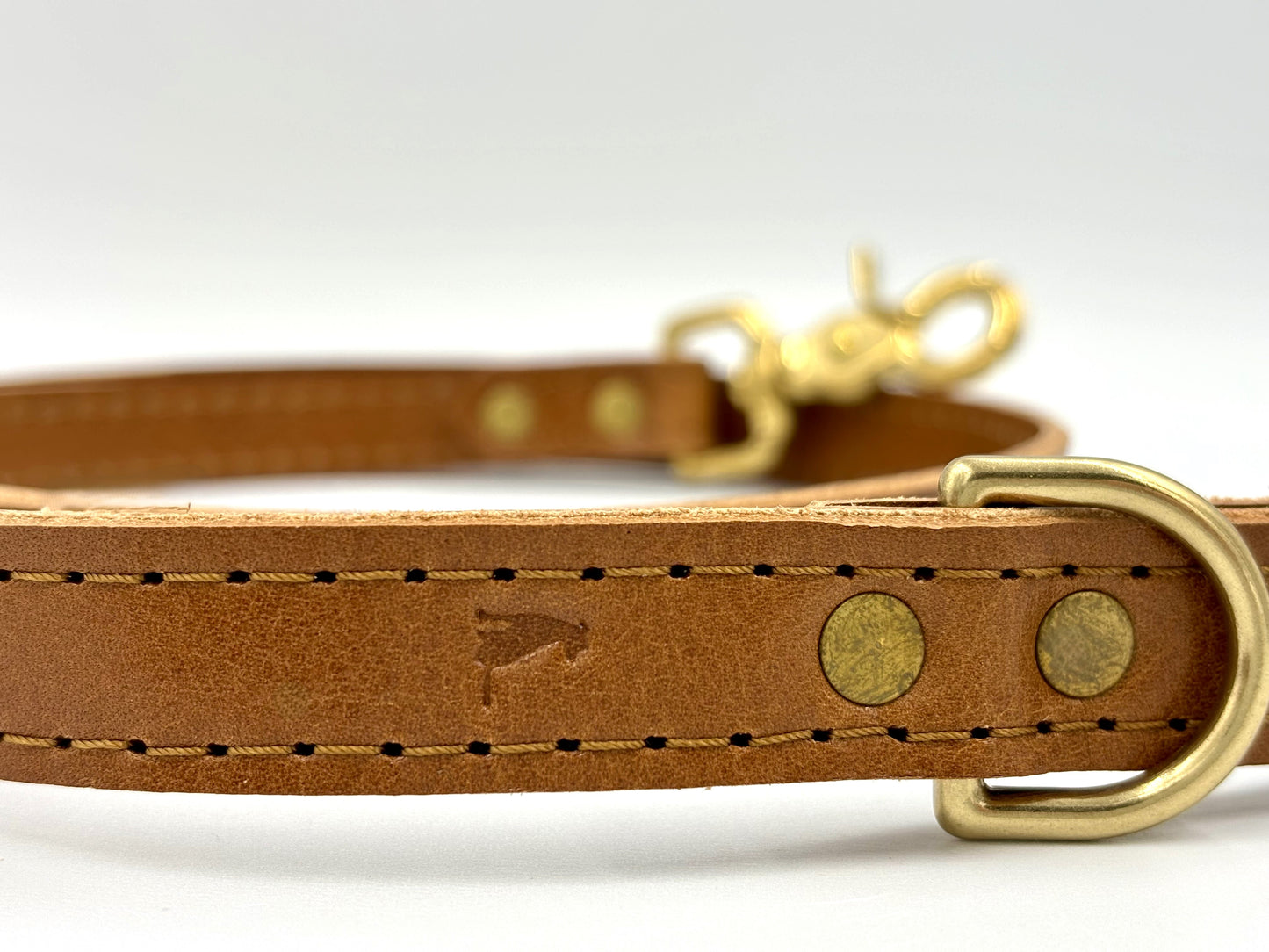 Close-up of caramel leather dog leash with golden brass hardware, highlighting its premium craftsmanship and elegant design.